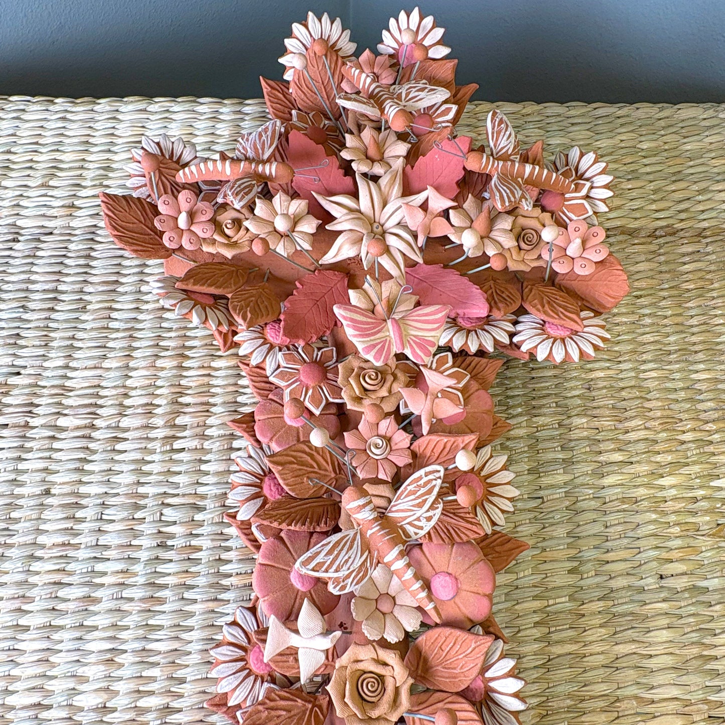 Handmade Mexican pottery clay cross, likely used for wall decor and featuring intricate floral, leaf and butterflies details.