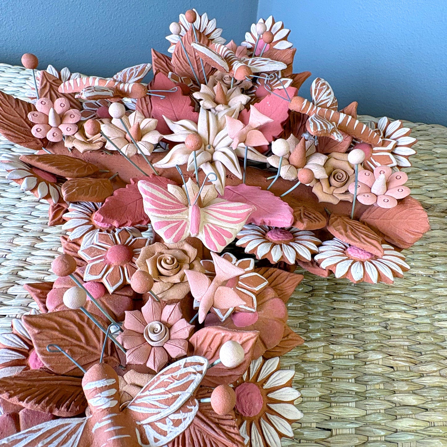 Handmade Mexican pottery clay cross, likely used for wall decor and featuring intricate floral, leaf and butterflies details.